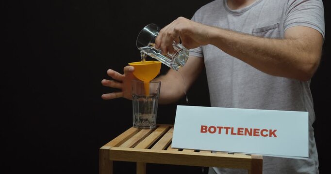 Man pouring water through a funnel beside a &ldquo;Bottleneck&rdquo; sign, illustrating workflow constraints, limited capacity, process delays and production optimization.