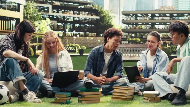 Portrait shows classmates in study session sitting on campus lawn for group study collaboration, reading notes from devices and books, with international peers in an academic environment.