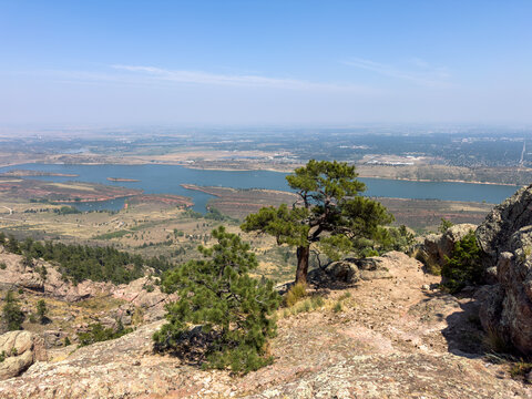 View of Arthur's Rock with pine trees and rocky terrain overlooking Horsetooth Reservoir under a clear blue sky in Fort Collins, Colorado, United States.