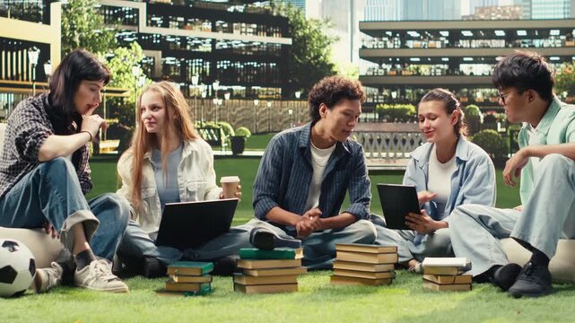 Portrait shows diverse students sitting on a university campus lawn for group study collaboration, reading notes from a laptop and books, with international peers in an academic environment.