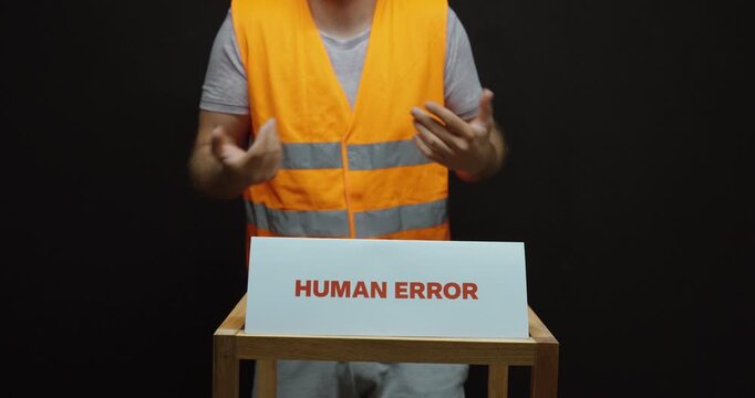 Worker gesturing and pointing at himself behind a &ldquo;Human Error&rdquo; sign, illustrating personal responsibility, workplace mistakes, accountability and manufacturing errors.