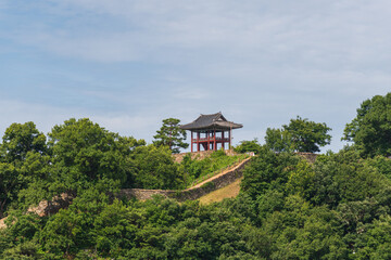 Fototapeta premium Traditional Korean pavilion above a historic stone fortress wall surrounded by lush summer forest in South Korea.