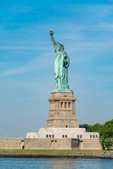 Statue of Liberty overlooks New York Harbor on July 4. Vertical telephoto view frames the copper monument, stone pedestal, blue sky and Liberty Island waterfront. © white78