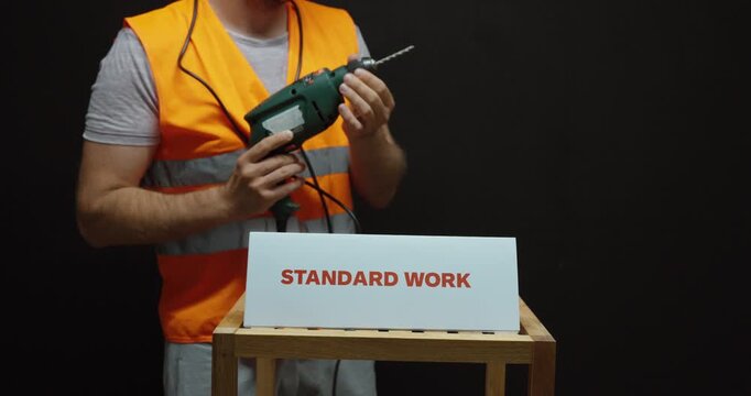 Industrial worker holding a power drill beside a &ldquo;Standard Work&rdquo; sign, representing standardized procedures, lean manufacturing, workplace efficiency and process consistency.