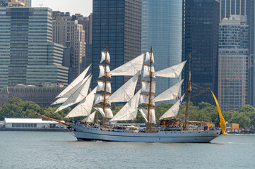BAE Guayas sails before Lower Manhattan on Independence Day. Ecuadorian Navy barque carries white sails and a yellow stern flag against dense waterfront office towers. © white78
