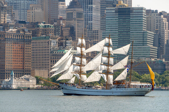 BAE Guayas sails beneath Lower Manhattan towers on July 4. Vertical telephoto view shows the Ecuadorian barque with white sails against historic and glass buildings.