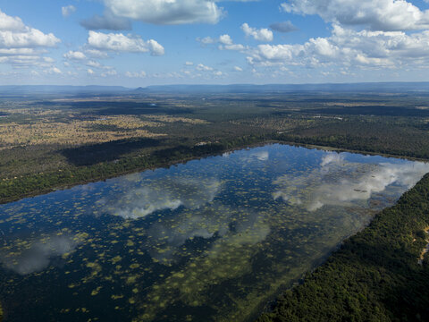 Aerial view of Neak Poan Temple surrounded by the vast baray waters, lush green forest, and reflections of clouds in the water in Krong Siem Reap, Siem Reap Province, Cambodia.