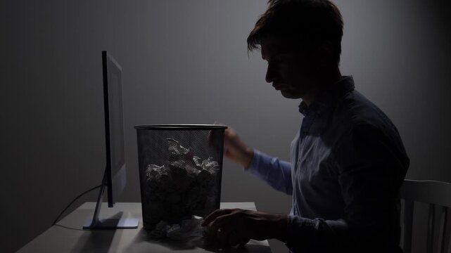 Stressed office worker sitting at a desk, throwing crumpled documents into a trash can, expressing frustration and disappointment with a difficult business problem or mistake