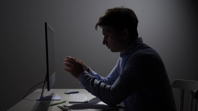 Man struggling with burnout and frustration, working late hours in a dark office, holding a crumpled paper while looking at the computer screen