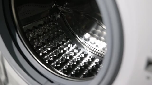 Close-up dolly shot inside washing machine drum. Detailed interior view of a new, empty washing machine with a camera slowly moving into the shiny, perforated stainless steel drum, highlighting modern