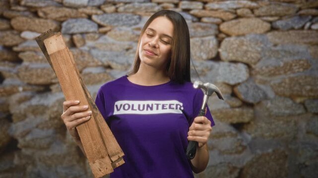 Woman holding hammer and wooden planks in stone building volunteer repair site; community service hopeful.