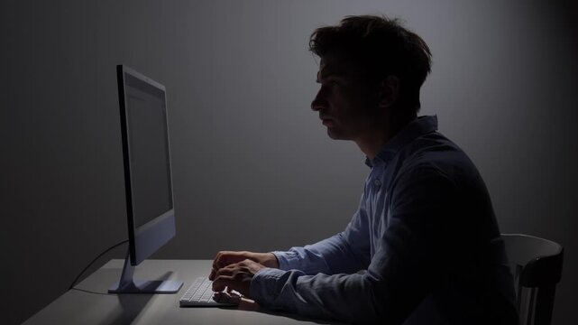 Man typing on a computer keyboard, focusing on the screen in a dimly lit room, symbolizing dedication, overtime, productivity, concentration, stress, and technology use