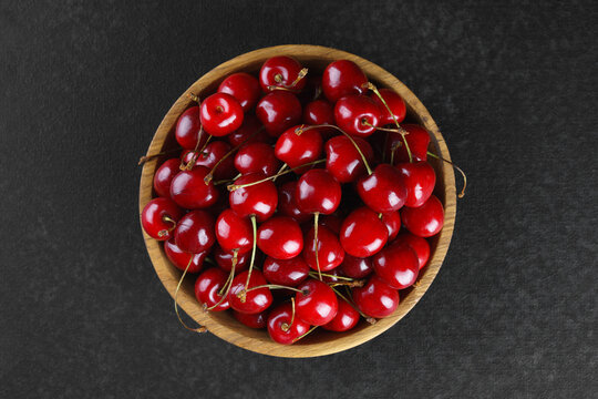 Fresh ripe sweet cherries in rustic wooden bowl on black stone textured background with copy space for text. Juicy organic summer fruit, red berries, healthy seasonal food, farm harvest