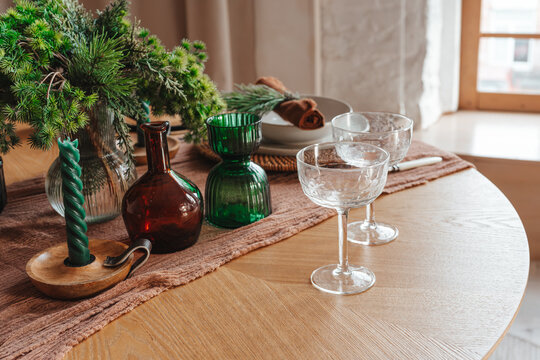 Elegant festive table setting with empty glasses, evergreen branches, candles and dinnerware on a wooden table, creating a warm atmosphere for Christmas or holiday celebrations.
