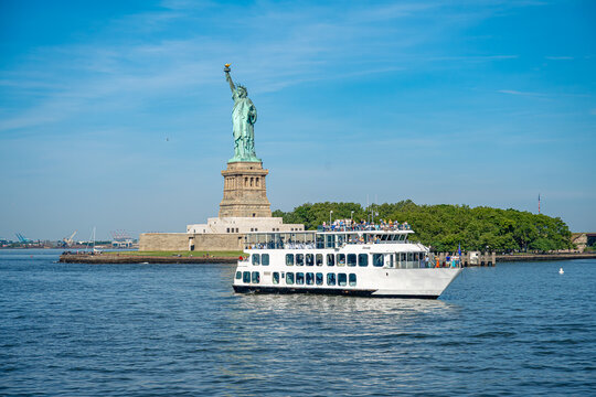 New York, USA, 4 Jule 2026 : White passenger boat sailing near Statue of Liberty in New York. Cruise vessel transports tourists on Hudson River during sunny summer day.