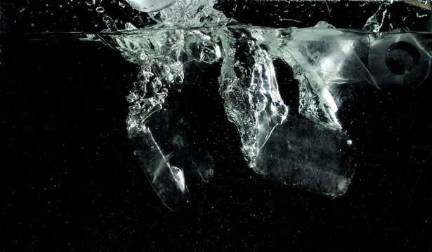 Falling ice tube pieces with water splashing in midair on a transparent, isolated black background. Ice tubes drop into water with air bubbles scatter splashing