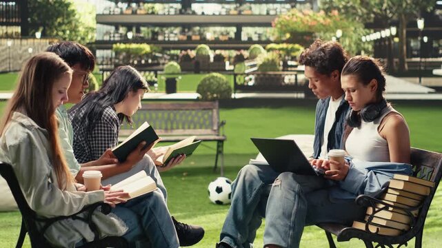 Students read project notes together on a wooden bench at a university campus, supporting peer tutoring, teamwork and collaborative academic learning during a focused group study session.