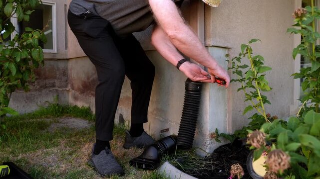 Senior homeowner fastening a flexible drainage pipe to the downspout of of his home
