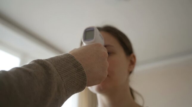 Young caucasian woman getting her temperature checked with an infrared thermometer on her forehead
