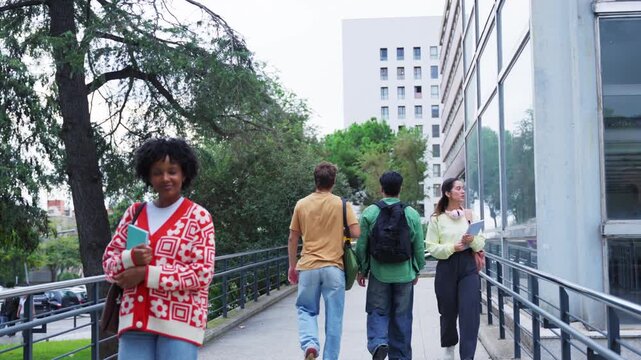 Young man and woman greeting each other with a smile while walking on the university campus, happy students enjoying a beautiful day after class with friends in the background