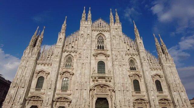 Majestic facade of the duomo di milano, a stunning example of gothic architecture with intricate spires and statues against a beautiful blue sky with scattered clouds in lombardy, italy