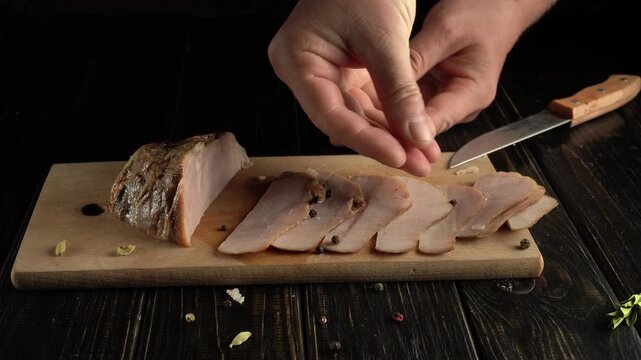Chef's hands sprinkle black pepper over sliced meat on a wooden cutting board, with a knife and whole spices visible, creating a culinary scene in a well-lit kitchen environment