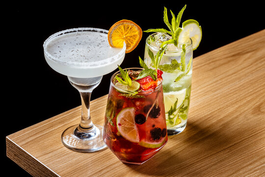 A delicious group of three craft cocktails: Margarita, Berry Smash, and Mojito on a wooden bar counter