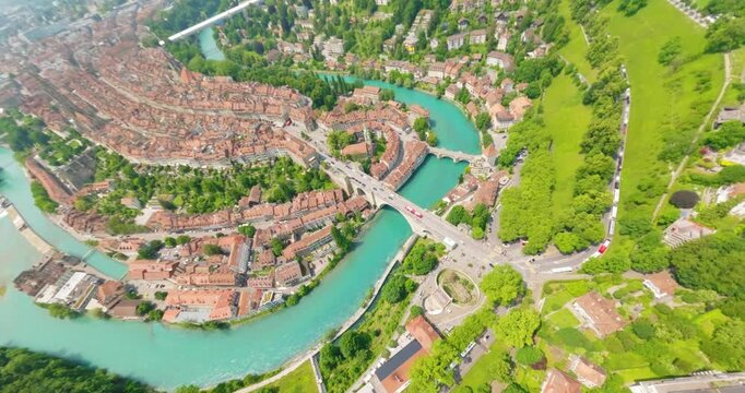 FPV aerial view of the Aare river flowing through the historic city of Bern with lush green trees and urban architecture in Switzerland.