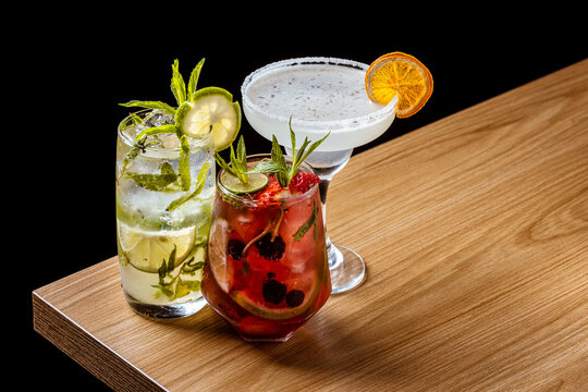 A delicious group of three craft cocktails: Margarita, Berry Smash, and Mojito on a wooden bar counter
