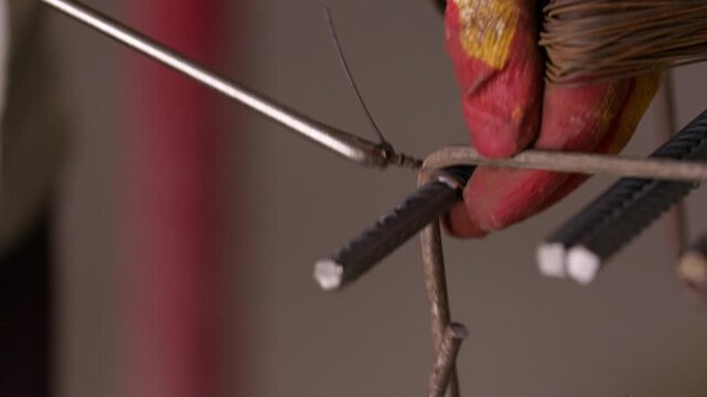 Worker tying steel reinforcement bars with binding wire close up