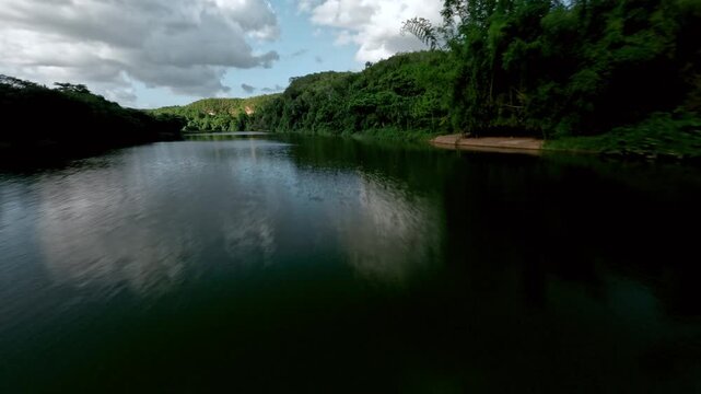 FPV aerial view of Chavon River flowing through lush green landscape with rocky banks and a bridge La Romana, La Romana, Dominican Republic.