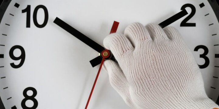 Gloved hand setting clock hands forward daylight saving time concept closeup