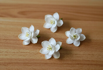 Obraz premium Four delicate white flowers with yellow stamens arranged on a light brown wooden surface, natural beauty and simplicity