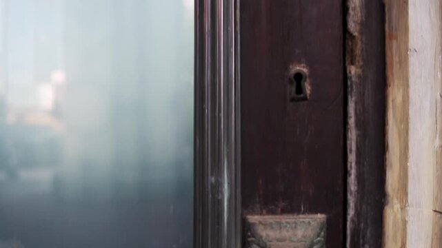 Vertical pedestal camera motion moving upward showing a close up of an antique bronze handle on an old vintage wooden door.