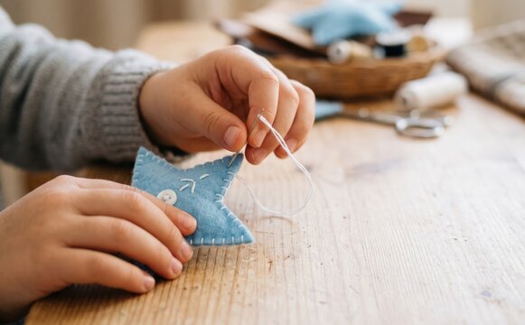 Child hands sewing a blue felt star toy on a wooden table crafting handmade Christmas ornament