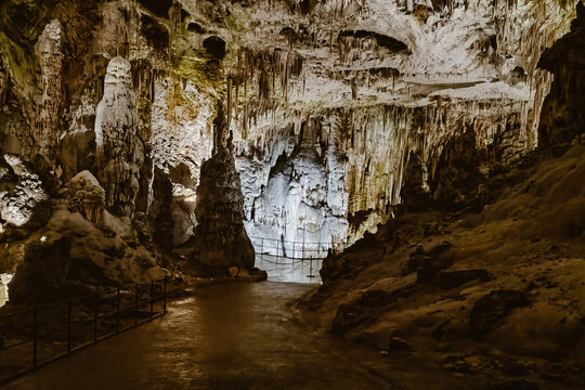 View of the illuminated limestone formations and stalactites inside the Postojna Cave with a walking path and metal railings in Postojna, Postojna, Slovenia.