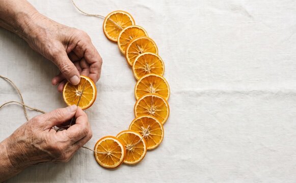 Elderly woman stringing dried orange slices into a rustic garland for handmade Christmas decor