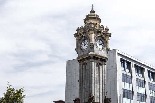 View of the ornate stone clock tower with detailed clock faces set against a modern building and a cloudy sky in Exeter, England, United Kingdom.