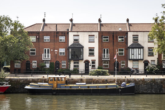 View of a narrowboat moored on the water in front of traditional red brick and white terraced houses along the historic harbourside in Bristol, England, United Kingdom.