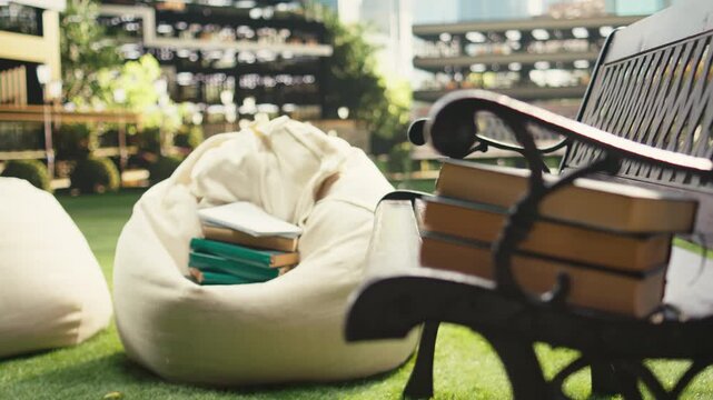 Close-up shows multiple stacked books and study materials on a wooden bench outdoors at a modern campus, creating an empty academic learning setup with literature, research tools and notebooks.