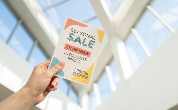 Person holding a seasonal sale flyer with special offer discounts inside for retail marketing
