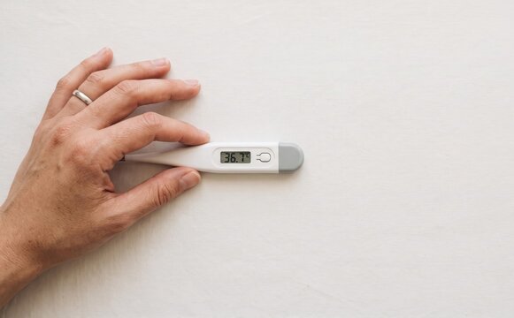 Person holding digital thermometer showing normal body temperature of thirty six point seven degrees for health check