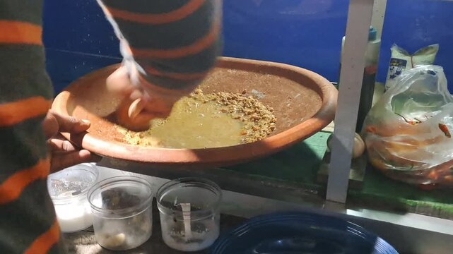 Street food vendor preparing Tahu Tek, a traditional East Javanese dish. Close up of cutting fried tofu, omelet, rice cakes using scissors, mixing rich peanut sauce. SUMENEP, INDONESIA - MAY 27, 2026