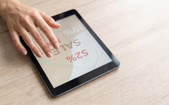 Woman shopping online for sale deals using digital tablet on wooden table