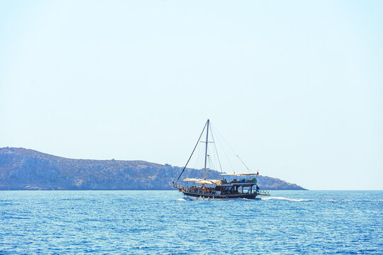 Traditional wooden sailing gulet anchors on calm blue sea with green coastal hills in the background.