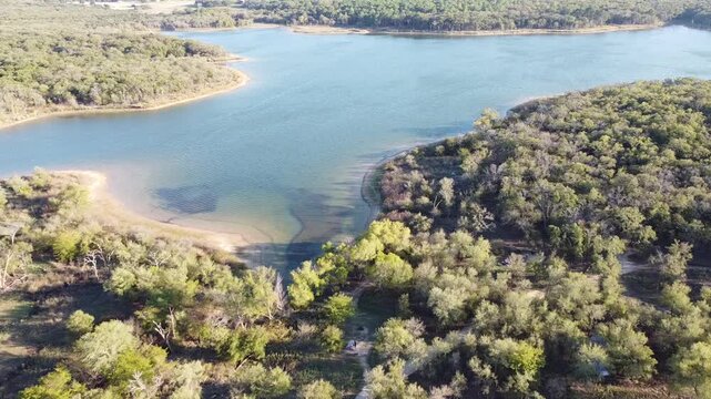 Lakeside woodland borders clear water inlets near Hawthorn Circle in Lake Ray Roberts State Park. Sandy paths wind through dense green canopy along peaceful cove environment, Pilot Point, TX