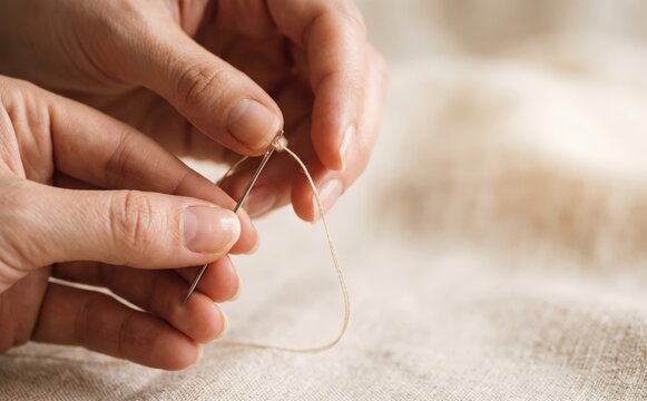 Close up of female hands threading a needle with beige yarn for sewing and embroidery craft