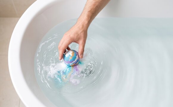 Hand dropping a colorful bath bomb into water in a white bathtub representing relaxation and spa care