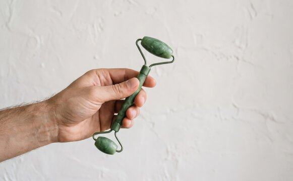 Man holding green jade facial roller for skin care and massage routine close up