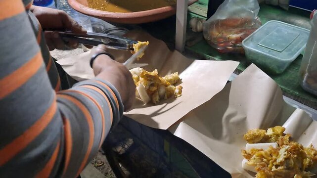 Street food vendor preparing Tahu Tek, a traditional East Javanese dish. Close up of cutting fried tofu, omelet, rice cakes using scissors, mixing rich peanut sauce. SUMENEP, INDONESIA - MAY 27, 2026